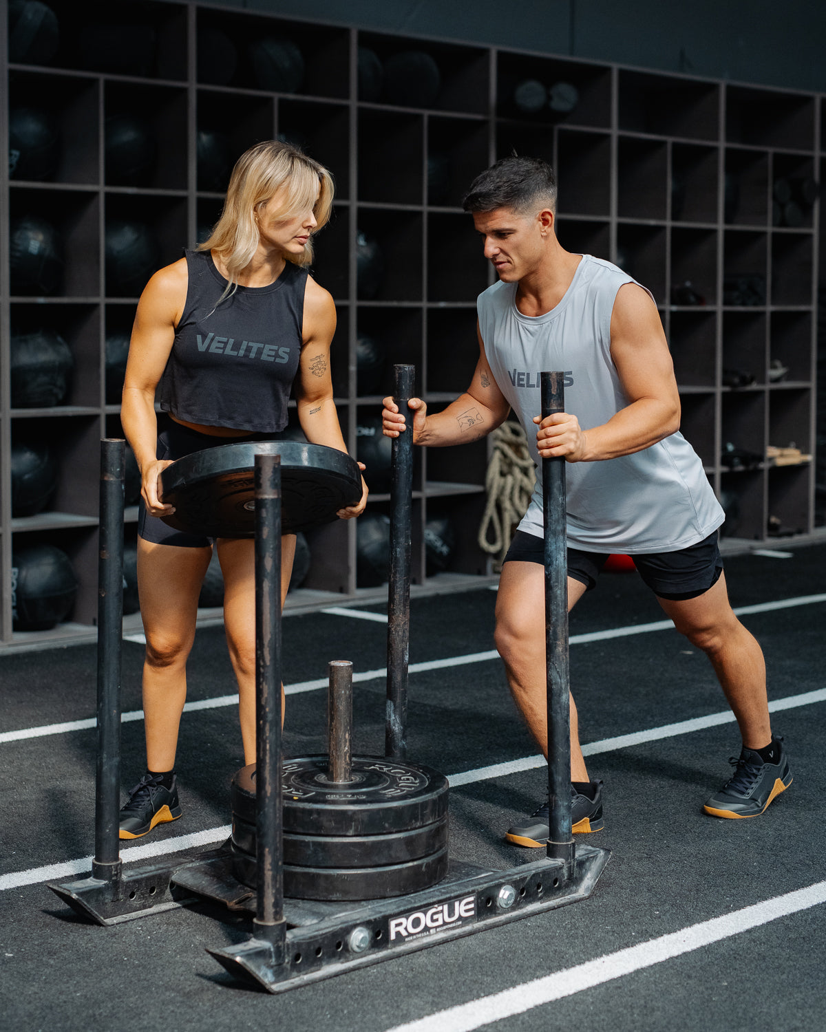 Athletes training in a box with a weighted sled, the athlete wears a Velites tank top